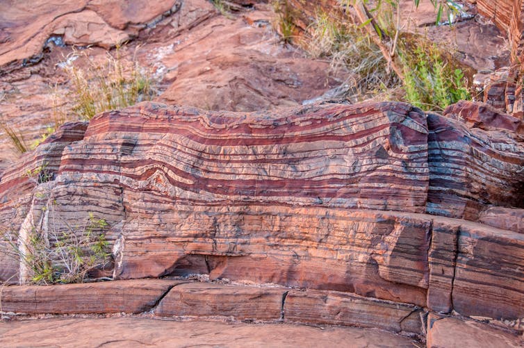 A rusty red rock with darker bands of red visible throughout.